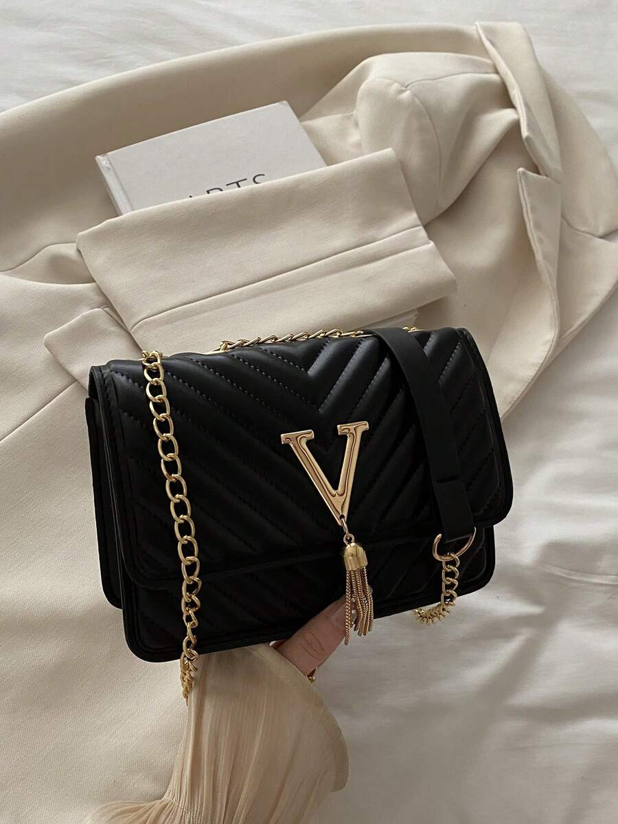 Refined Embossed Letter Shoulder Bag – New Year Collection in black with gold chain strap and elegant tassel detail.