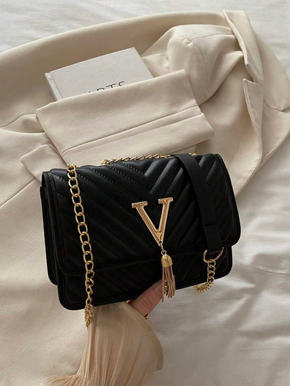 Refined Embossed Letter Shoulder Bag – New Year Collection in black with gold chain strap and elegant tassel detail.